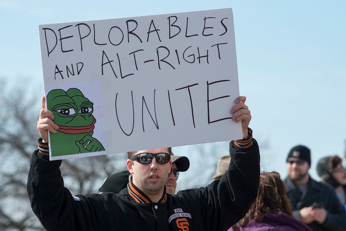 An alt-right protestor holds a sign depicting Pepe the Frog
