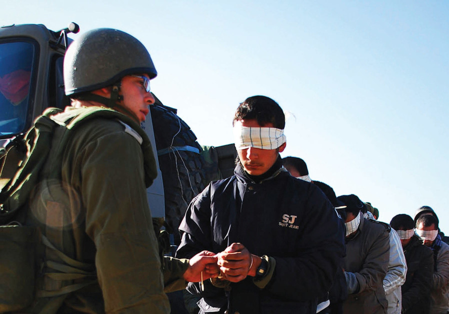 An IDF soldier stands next to a blindfolded Palestinian prisoner