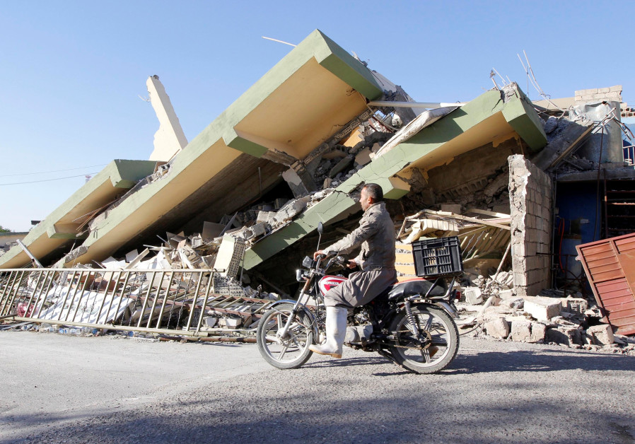 A man rides past the remains of a building in Darbandikhanm, Kurdistan, after a 7.2 magnitude earthq
