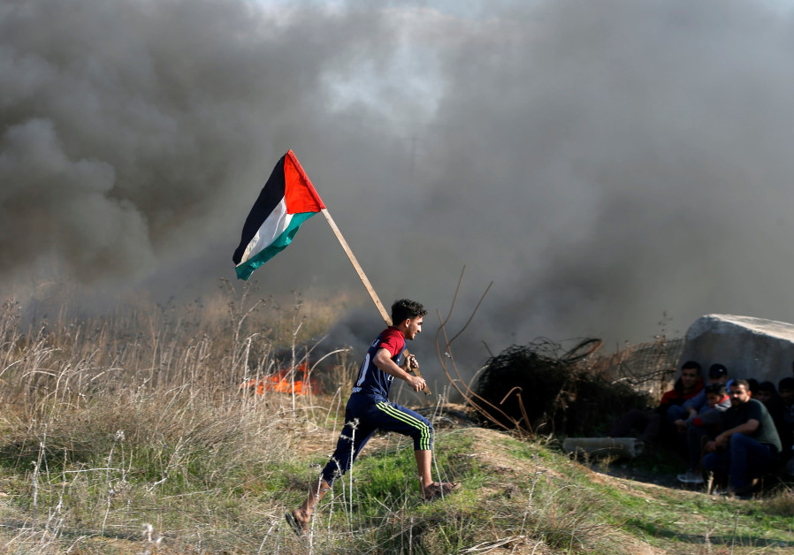 A protester holds a Palestinian flag as he runs during clashes with Israeli troops