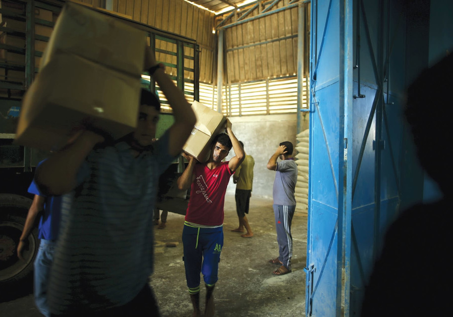 WORKERS CARRY boxes containing food supplies for Palestinian refugees at a United Nations Relief and