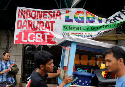 A street vendor walks past a banner reading 'Indonesia LGBT Emergency'