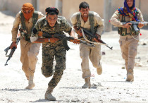 KURDISH FIGHTERS from the People’s Protection Units (YPG) run across a street in Raqqa, Syria in Jul