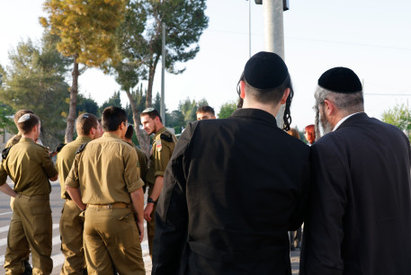  Haredi men dressed in traditional ultra-Orthodox garb stand behind a group of religious IDF soldiers