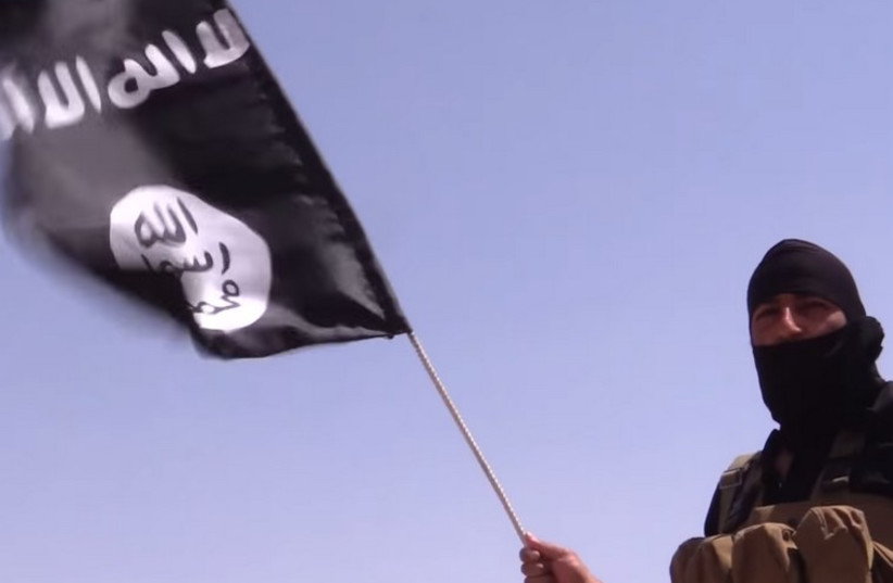 An Islamic State terrorist holds a flag with the group's insignia. (photo credit: REUTERS)