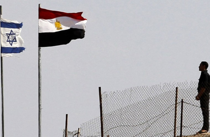 An Egyptian soldier stands near the Egyptian national flag and the Israeli flag at the Taba crossing between Egypt and Israel (photo credit: REUTERS)