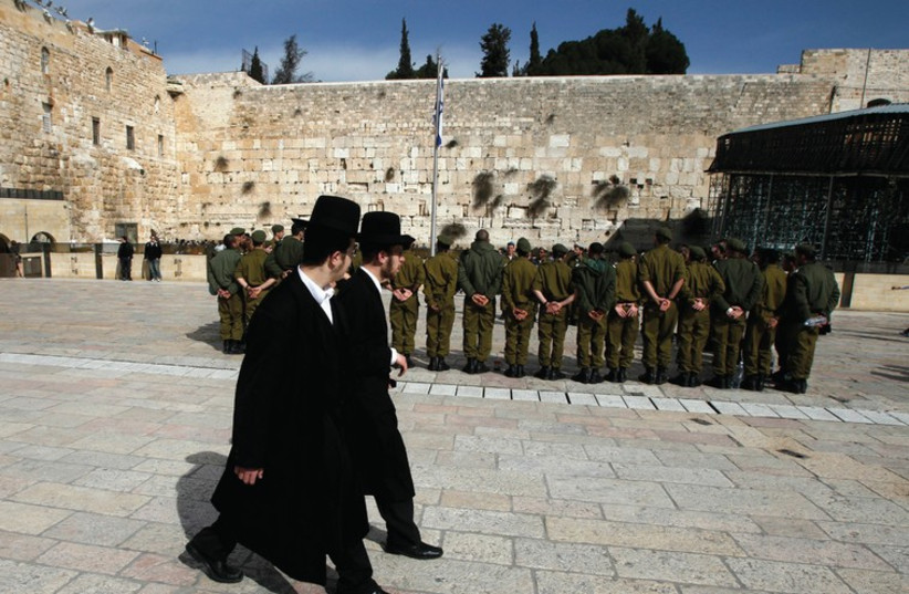 ULTRA-ORTHODOX MEN walk past soldiers at the Kotel in Jerusalem (photo credit: REUTERS)