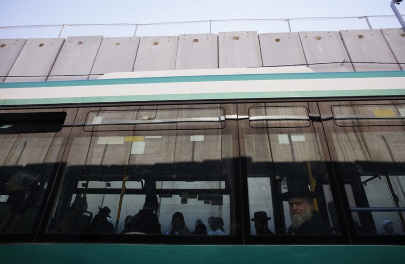 Jewish worshippers board a bus next to a section of the controversial Israeli barrier after visiting Rachel's Tomb in Bethlehem (photo credit: REUTERS)
