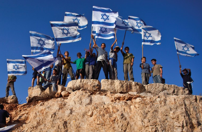 Jewish Youths in Israel wave flags and stand atop a hill. The author recalls his own young days in Zionist youth groups. (photo credit: REUTERS)