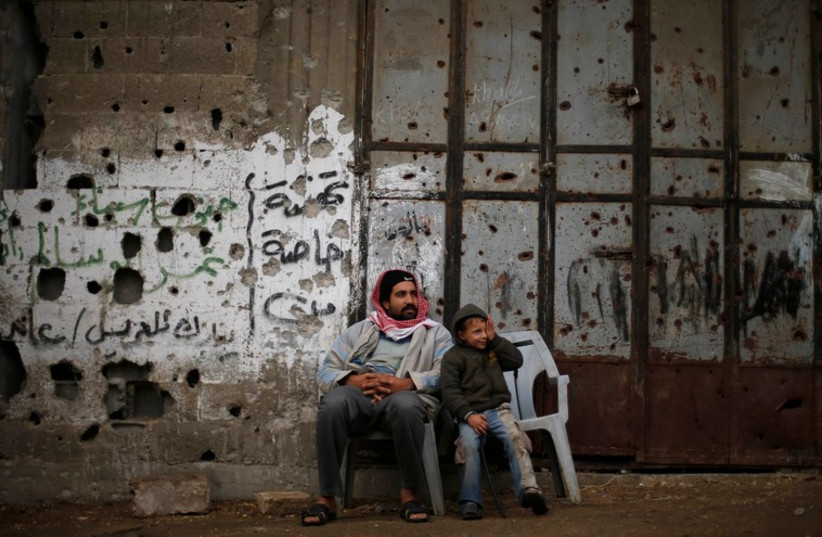 A Palestinian man sits with his son outside their house, that witnesses said was damaged by Israeli shelling during a 50-day war last summer, in the east of Gaza City January 7 (photo credit: REUTERS)