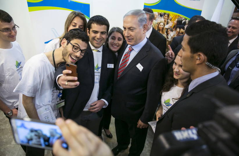 Israel's Prime Minister Benjamin Netanyahu (C) has his photo taken with members of Masa before attending a weekly cabinet meeting at his office in Jerusalem March 30, 2014. Masa is a programme that provides educational trips in Israel for young Jewish adults. (photo credit: BAZ RATNER/REUTERS)