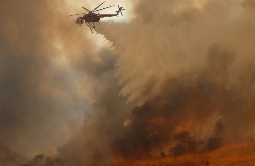 A helicopter drops water on a wind driven wildfire. (photo credit: REUTERS)