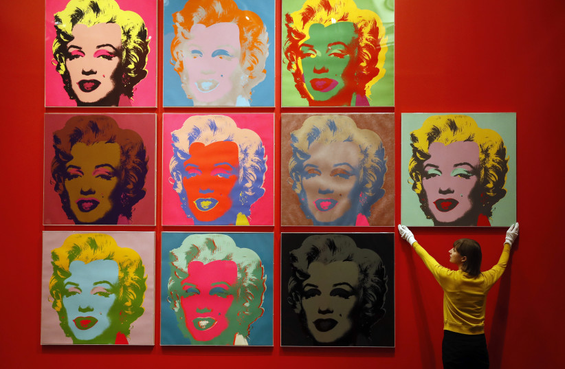 An employee poses with ten screenprints of Marilyn Monroe by Andy Warhol (photo credit: REUTERS)