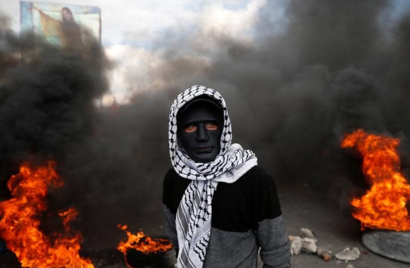 A Palestinian demonstrator stands near burning tires during clashes with Israeli troops at a protest against US President Donald Trump's decision to recognise Jerusalem as the capital of Israel, near the West Bank city of Nablus December 15, 2017 (photo credit: REUTERS/MOHAMAD TOROKMAN)