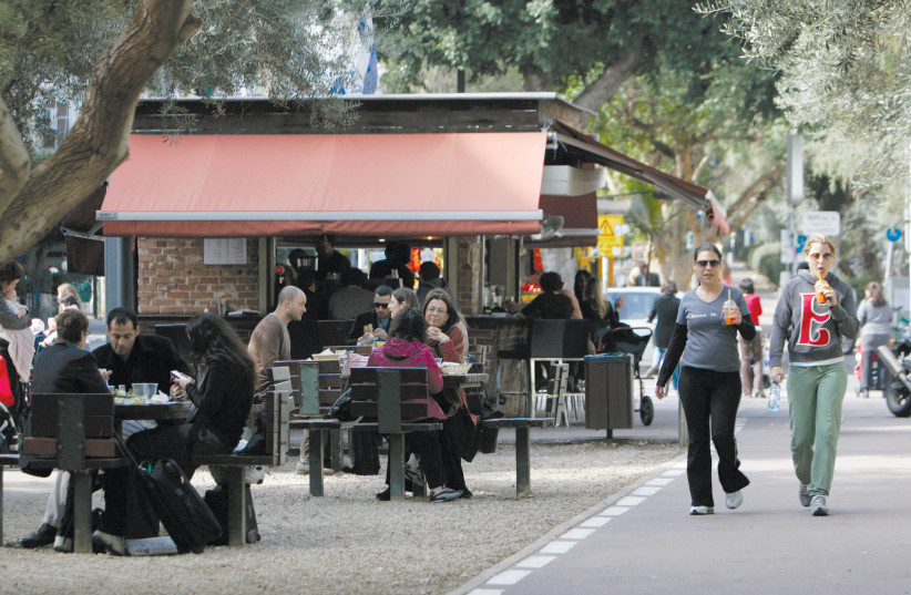 PEOPLE WALK past a cafe in Tel Aviv (photo credit: SHARON PERRY/REUTERS)