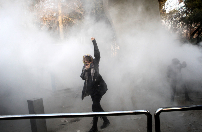 An Iranian woman raises her fist amid the smoke of tear gas at the University of Tehran during a protest on December 30, 2017 (photo credit: STR / AFP)