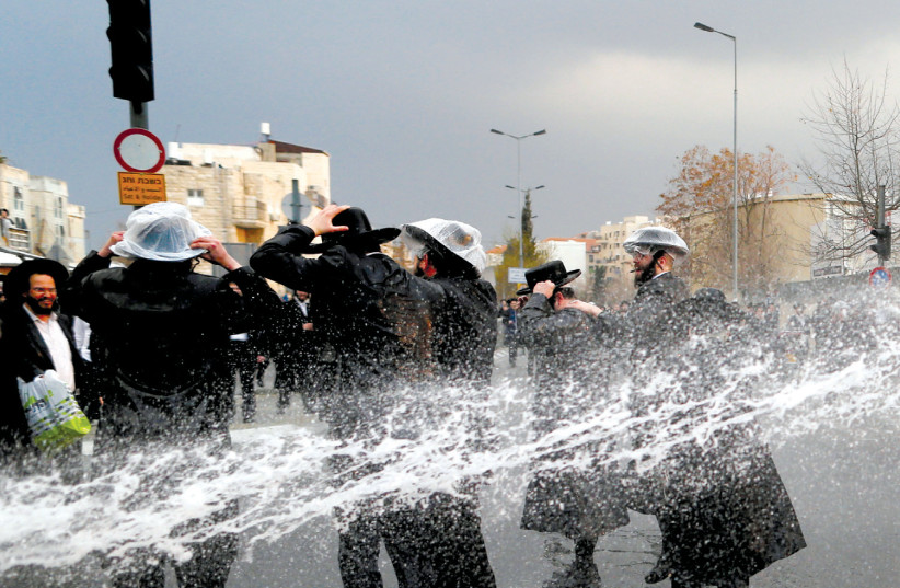 HAREDI protesters are sprayed with water by police as they block a street during a demonstration in Jerusalem against members of their community serving in the IDF, part of ongoing demonstrations (photo credit: AMMAR AWAD/REUTERS)