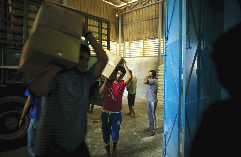 WORKERS CARRY boxes containing food supplies for Palestinian refugees at a United Nations Relief and Work Agency (UNRWA)-run food distribution center in Gaza in 2015. (photo credit: MOHAMMED SALEM/ REUTERS)