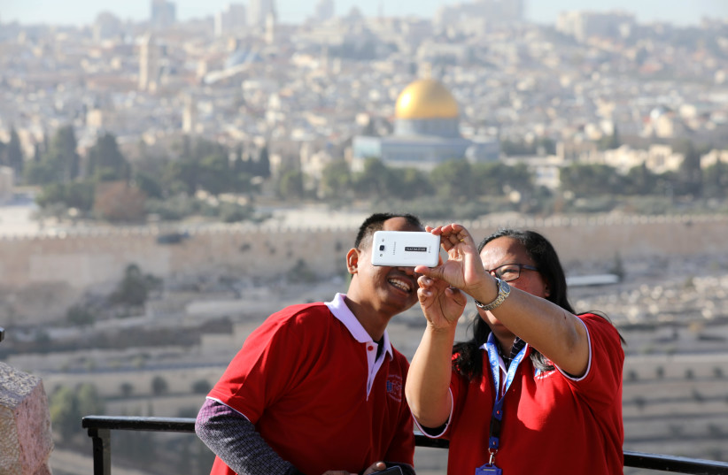 Tourists look at a mobile phone as they stand at an observation point overlooking the Dome of the Rock and Jerusalem's Old City (photo credit: AMMAR AWAD / REUTERS)