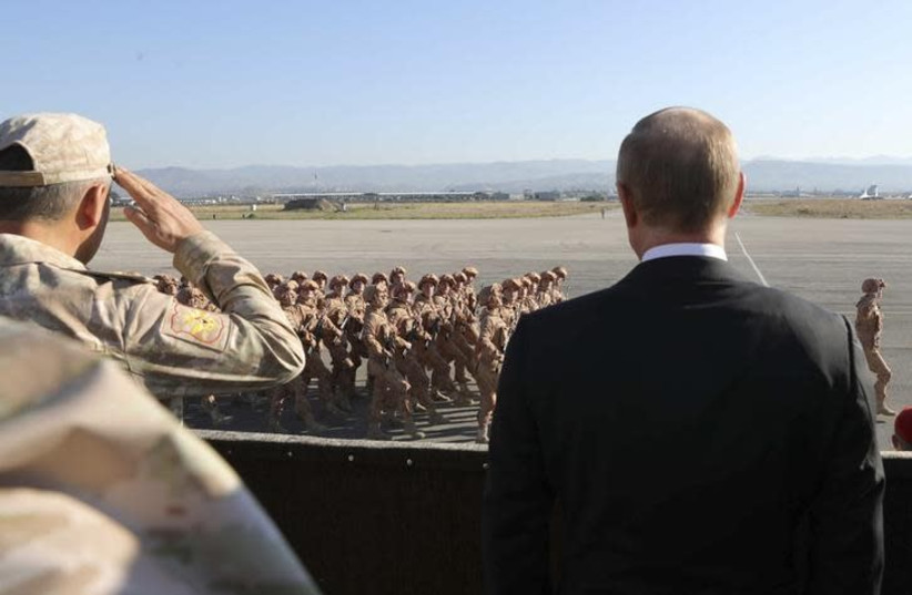 Russian President Vladimir Putin (R) and Defence Minister Sergei Shoigu watch servicemen passing by as they visit the Hmeymim air base in Latakia Province, Syria December 11, 2017 (photo credit: SPUTNIK/MIKHAIL KLIMENTYEV/KREMLIN VIA REUTERS)