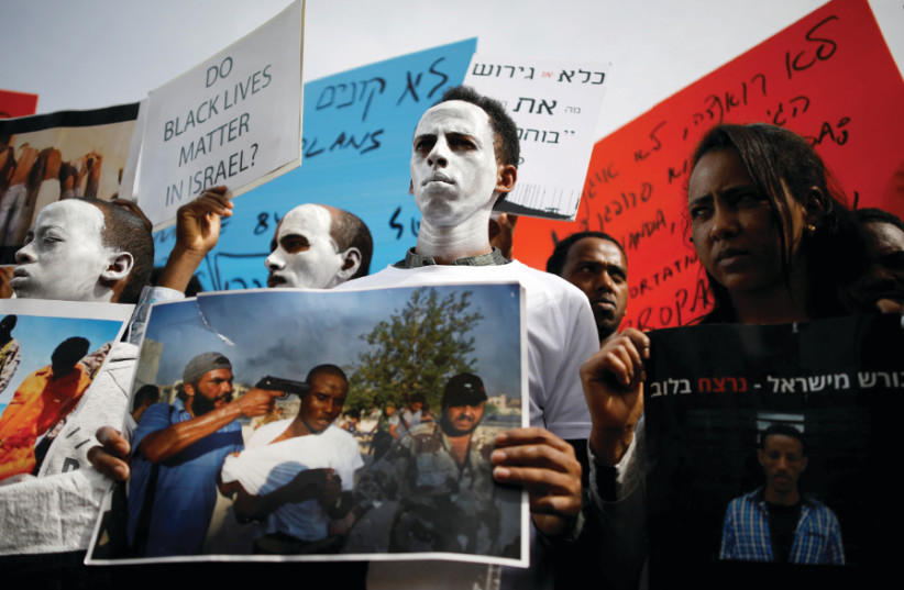 African migrants painted in white hold signs during a protest against the Israeli government's plan to deport part of their community, in front of the Rwandan embassy in Herzliya, Israel February 7, 2018 (photo credit: AMIR COHEN/REUTERS)