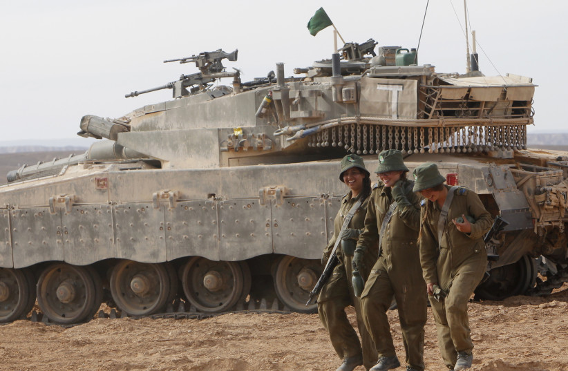 Israeli female soldiers walk in front of a tank during an exercise at the end of their tank instructors course at Shizafon base (photo credit: RONEN ZVULUN / REUTERS)