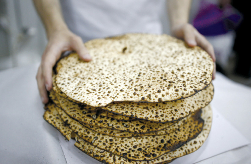 A MAN wraps fresh matza during Passover in Ashdod in 2016 (photo credit: AMIR COHEN/REUTERS)