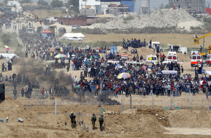 A picture taken on April 13, 2018 from the southern Israeli kibbutz of Nahal Oz across the border with the Gaza Strip shows Israeli soldiers keeping position and Palestinian protestors gathering along the border fence with Israel. Several thousand Gazans gathered for a third consecutive Friday of ma (photo credit: JACK GUEZ / AFP)