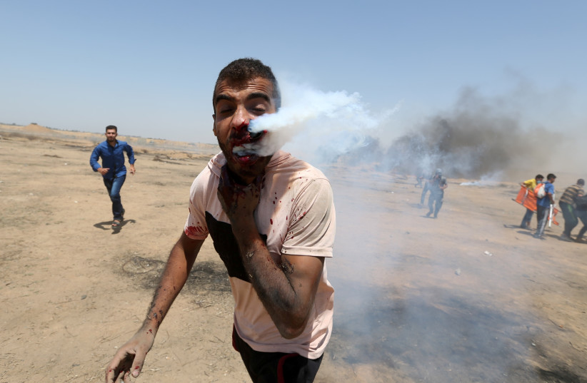 A wounded Palestinian demonstrator reacts as he is hit in the face with a tear gas canister fired by Israeli troops during a protest marking al-Quds Day, (Jerusalem Day), at the Israel-Gaza border in the southern Gaza Strip June 8, 2018. (photo credit: IBRAHEEM ABU MUSTAFA / REUTERS)