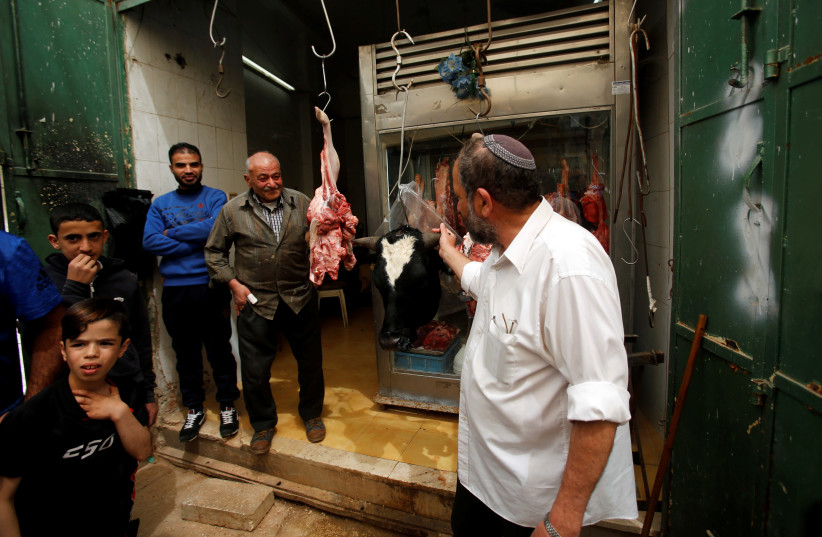 A Jewish man looks at meat at Palestinian butcher's shop in Hebron, in West Bank, 2018. (photo credit: REUTERS/MUSSA QAWASMA)
