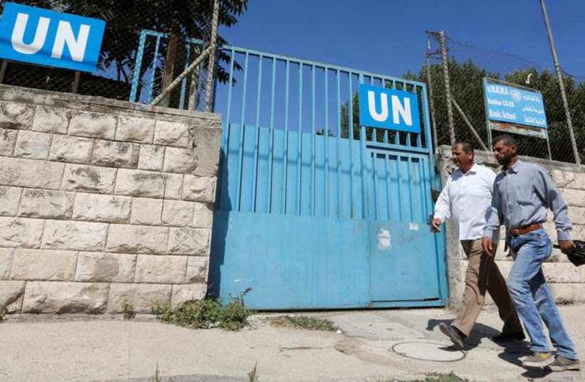 Palestinians pass by the gate of an UNRWA-run school in Nablus in the West Bank August 13, 2018 (photo credit: ABED OMAR QUSINI/REUTERS)