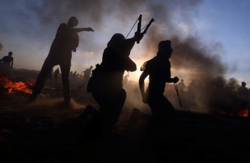 Palestinians hurl stones at Israeli troops during a protest at the Israel-Gaza border fence, in the southern Gaza Strip September 21, 2018 (photo credit: IBRAHEEM ABU MUSTAFA / REUTERS)