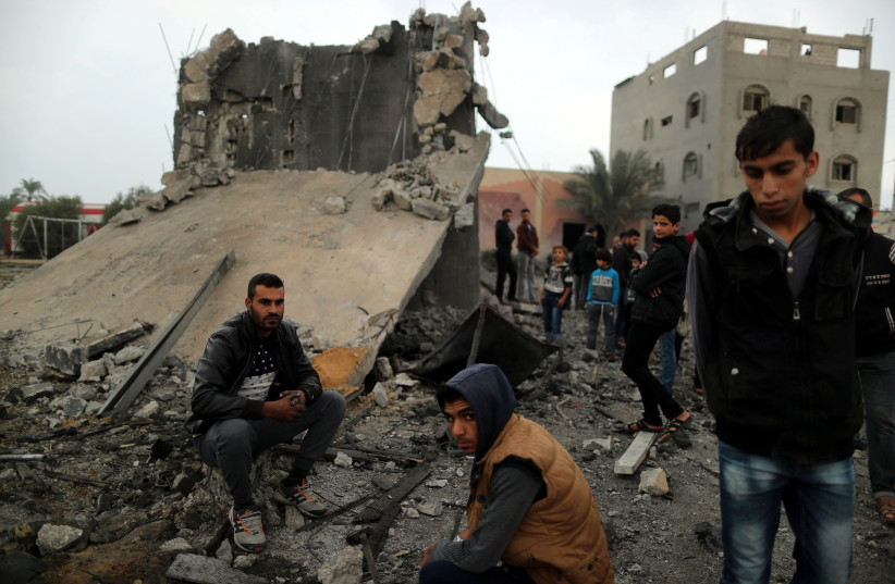 Palestinians sit at the remains of a building that was destroyed by an Israeli air strike, in Khan Younis in the southern Gaza Strip, November 12, 2018 (photo credit: SUHAIB SALEM / REUTERS)