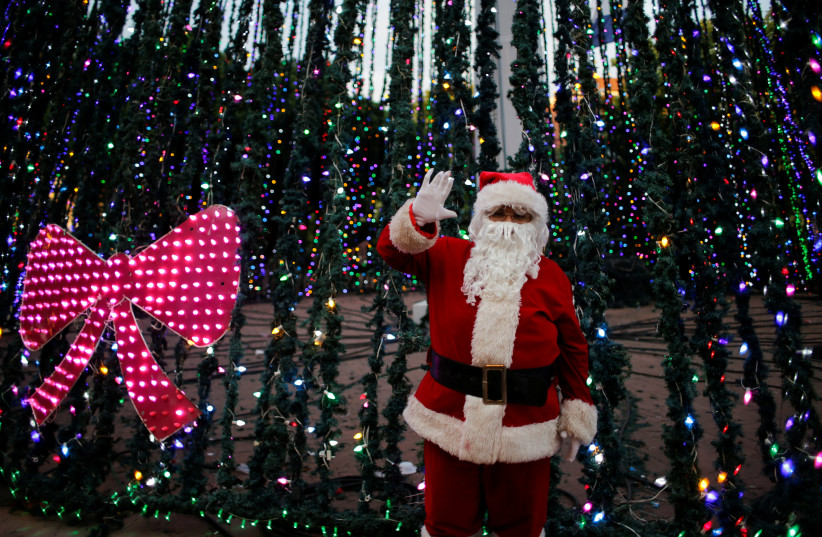 A man dressed as Santa Claus gestures in front of a Christmas tree (photo credit: OSWALDO RIVAS/REUTERS)