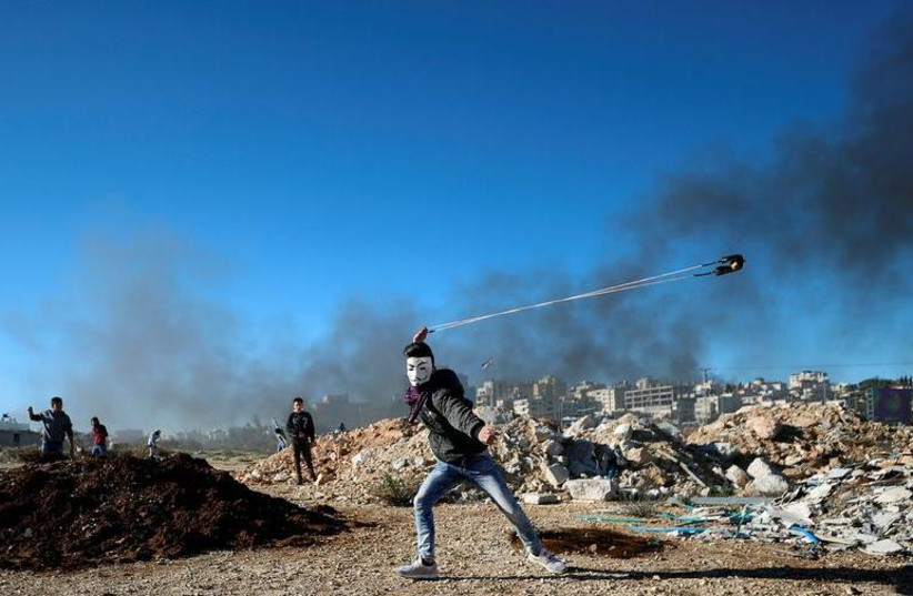 A Palestinian uses a sling to hurl stones during clashes with Israeli troops near the Jewish settlement of Beit El, near Ramallah, in the Israeli-occupied West Bank December 14, 2018.  (photo credit: REUTERS/MOHAMAD TOROKMAN)