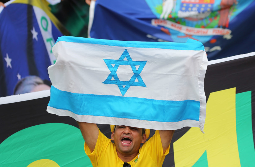 A man displays national flag of Israel as supporters of Brazil's new President Jair Bolsonaro gather outside the Planalto Palace ahead of Bolsonaro's swear-in ceremony, in Brasilia, Brazil, January 1, 2019.  (photo credit: SERGIO MORAES / REUTERS)