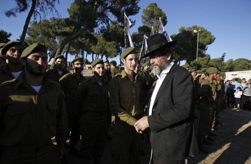 An ultra-Orthodox, or Haredi, Jewish man walks past Israeli soldiers of the Netzah Yehuda Haredi infantry battalion during their swearing-in ceremony in Jerusalem (photo credit: AMMAR AWAD/REUTERS)
