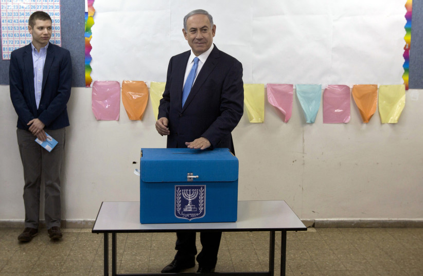 Israel's Prime Minister Benjamin Netanyahu casts his ballot for the parliamentary election as his son Yair stands behind him at a polling station in Jerusalem March 17, 2015. (photo credit: SEBASTIAN SCHEINER/POOL VIA REUTERS)