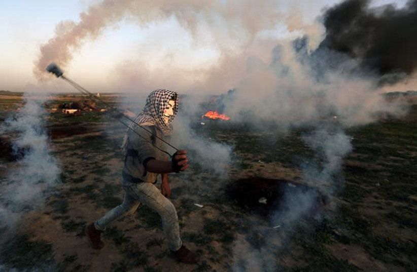 A Palestinian demonstrator uses a sling to hurl back a tear gas canister fired by Israeli troops during a protest at the Israel-Gaza border fence (photo credit: REUTERS/IBRAHEEM ABU MUSTAFA)