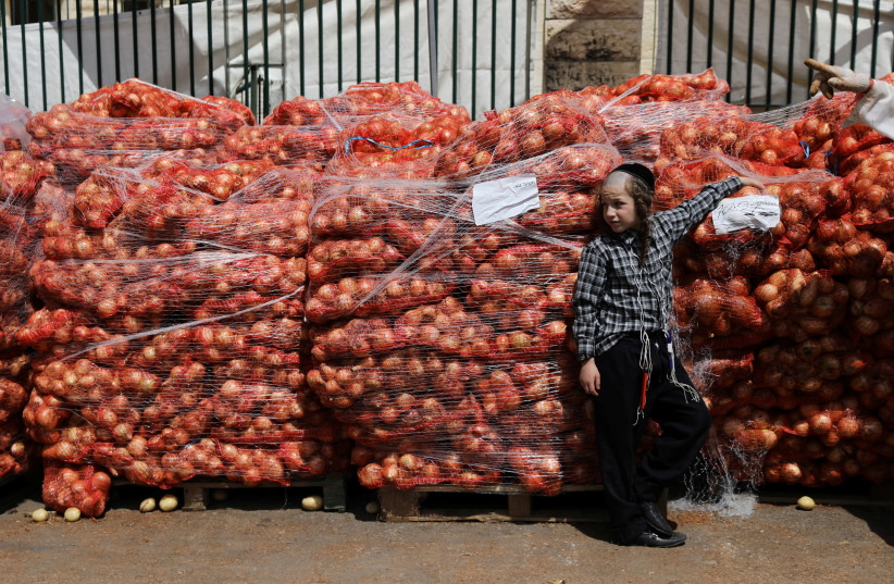 An ultra-Orthodox Jewish boy leans against sacks of onions at a food distribution center providing food products for families ahead of the upcoming Jewish holiday of Passover in Jerusalem's Mea Shearim neighbourhood, April 16, 2019 (photo credit: AMMAR AWAD / REUTERS)