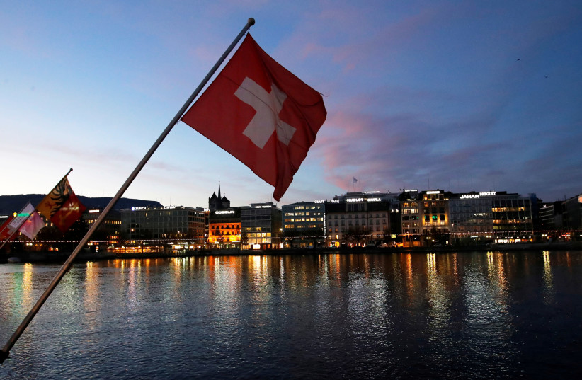 A Swiss flag is pictured during the sunrise on the Commercial and Financial District in Geneva, Switzerland, November 23, 2017 (photo credit: REUTERS/DENIS BALIBOUSE)
