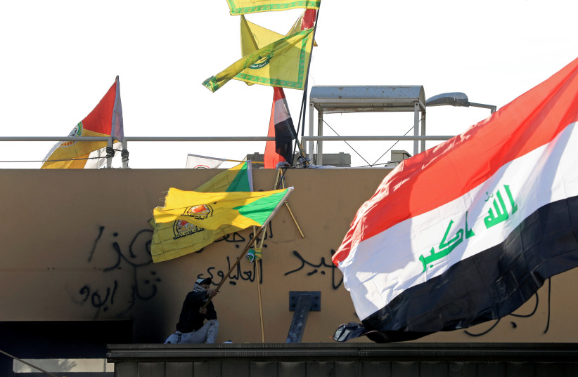 A member of Hashd al-Shaabi waves a flag of Kataib Hezbollah militia group during a protest to condemn air strikes on bases belonging to Hashd al-Shaabi (paramilitary forces), outside the U.S. Embassy in Baghdad (photo credit: REUTERS)