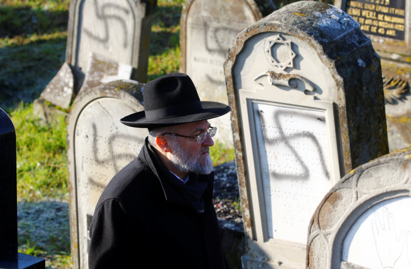 A man walks past graves desecrated with swastikas at the Jewish cemetery in Westhoffen, near Strasbourg, France, December 4, 2019. (photo credit: ARND WIEGMANN / REUTERS)
