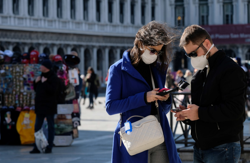 Tourists wear protective masks in Saint Mark's Square in Venice as Italy battles a coronavirus outbreak, Venice, Italy, February 27, 2020 (photo credit: REUTERS/MANUEL SILVESTRI)