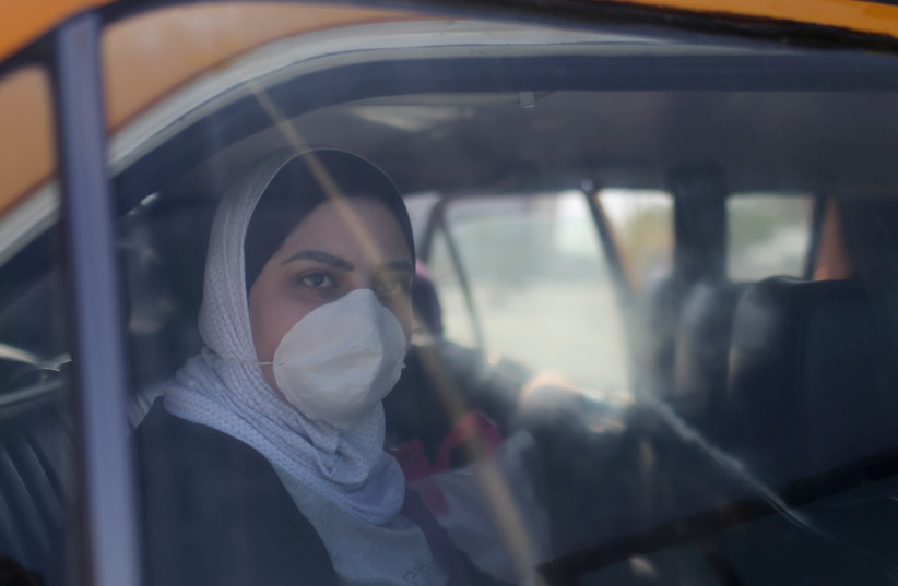 A Palestinian woman, wearing a mask as a preventive measure against coronavirus, looks out of a car upon her return from abroad, at Rafah border crossing in the southern Gaza Strip (photo credit: REUTERS)