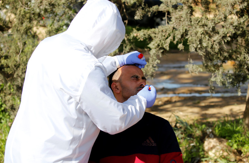 A member of medical staff swabs the nose of a Palestinian worker for coronavirus disease (COVID-19) testing upon his return from Israel, outside the Israeli-controlled Tarqumiya checkpoint near Hebron in the Israeli-occupied West Bank March 26, 2020 (photo credit: MUSSA QAWASMA / REUTERS)