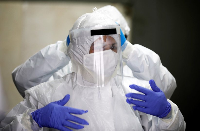 Employees of Chevra Kadisha, the main group that oversees Jewish burials in Israel, adjust their protective gear at a special centre that prepares bodies of Jews who died from the coronavirus disease (COVID-19) at a cemetery in Tel Aviv, Israel March 31, 2020 (photo credit: REUTERS/AMIR COHEN)