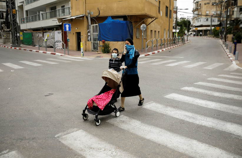 An ultra-Orthodox Jewish woman crosses a street with her children in Bnei Brak, a town badly affected by the coronavirus disease (COVID-19), and which Israel declared a "restricted zone" due to its high rate of infections, near Tel Aviv, Israel April 5, 2020 (photo credit: REUTERS/AMIR COHEN)