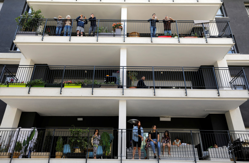 Residents stand on their balcony as they watch Israeli soldiers performing for them in a bid to assist civilians observing government stay-at-home orders to help fight the spread of the coronavirus disease (COVID-19) in Tel Aviv, Israel April 7, 2020. (photo credit: AMIR COHEN/REUTERS)