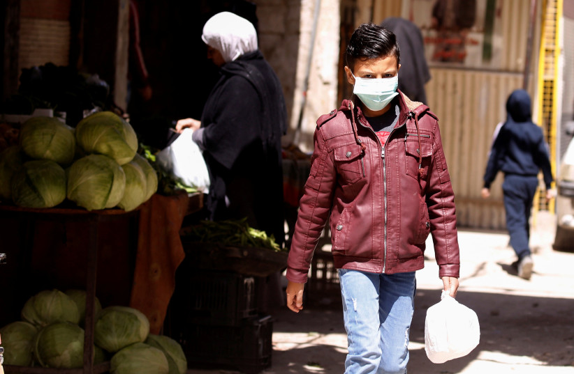 A boy wearing a face mask walks inside Jaramana Palestinian refugee camp, following the outbreak of coronavirus disease (COVID-19), in Damascus, Syria April 1, 2020 (photo credit: REUTERS/OMAR SANADIKI)